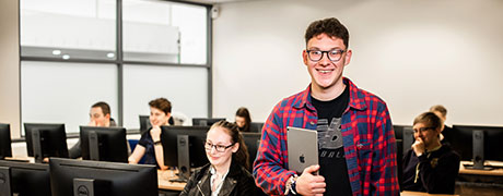 A student holding a laptop in a computer room