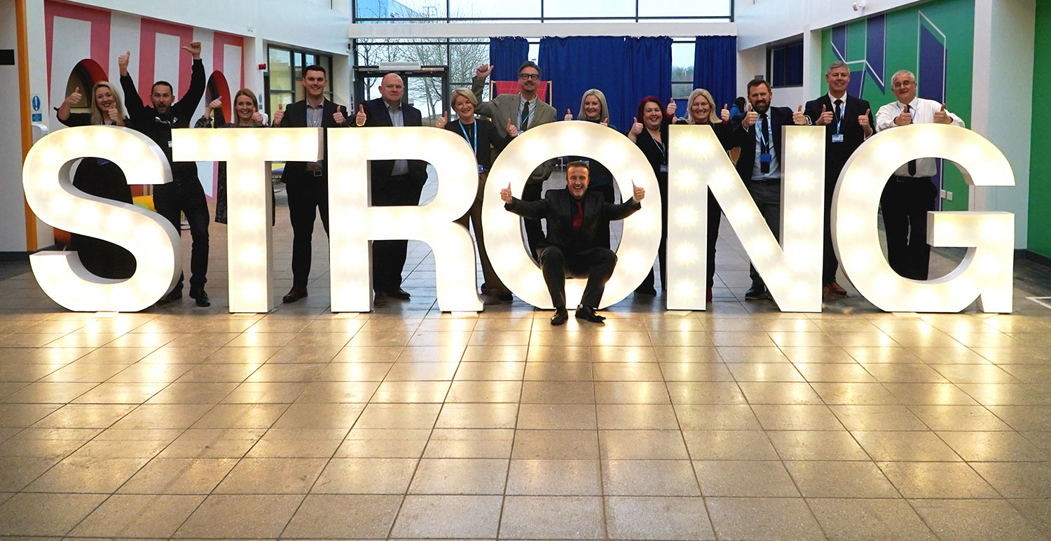 Staff standing around a large light installation that reads STRONG